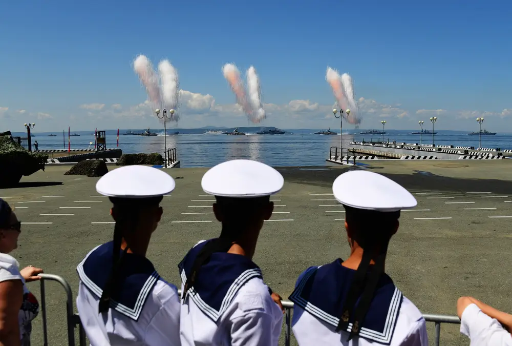 Navy sailors in uniform observe shipboard technical maneuvers and naval vessels during a maritime training exercise.