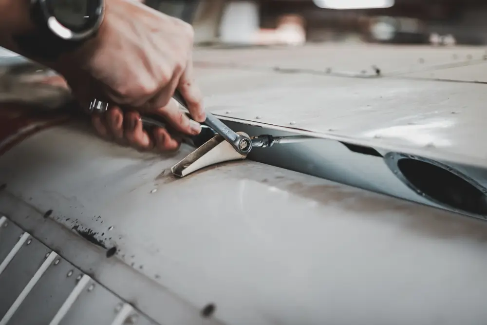 Aircraft maintenance airman technician using a wrench to perform mechanical repairs on a white aircraft panel.