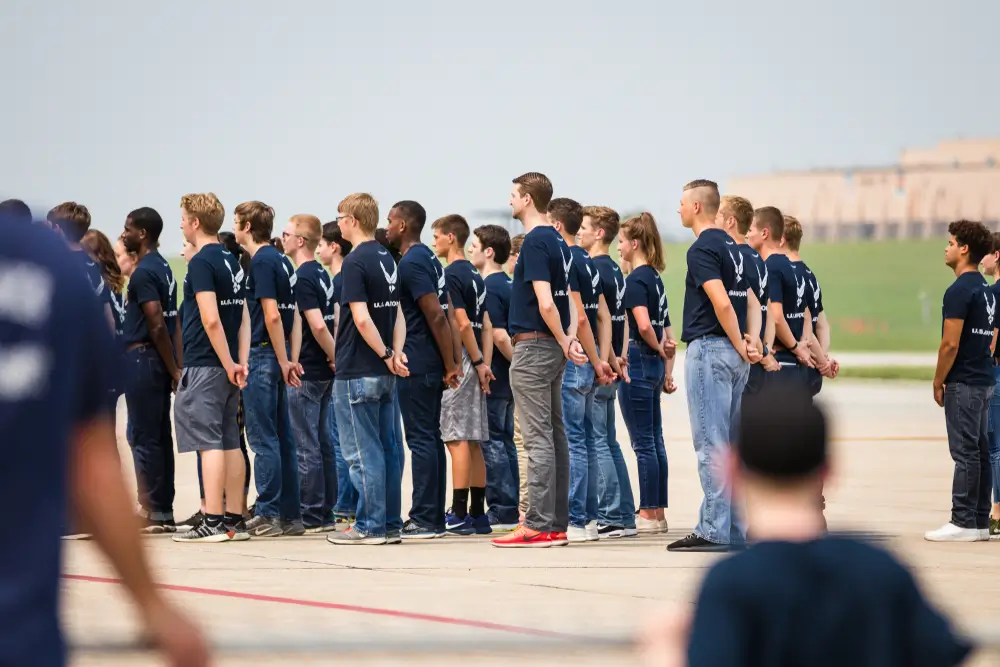Candidates in Air Force t-shirts standing in formation outdoors for military enlistment and aptitude testing.