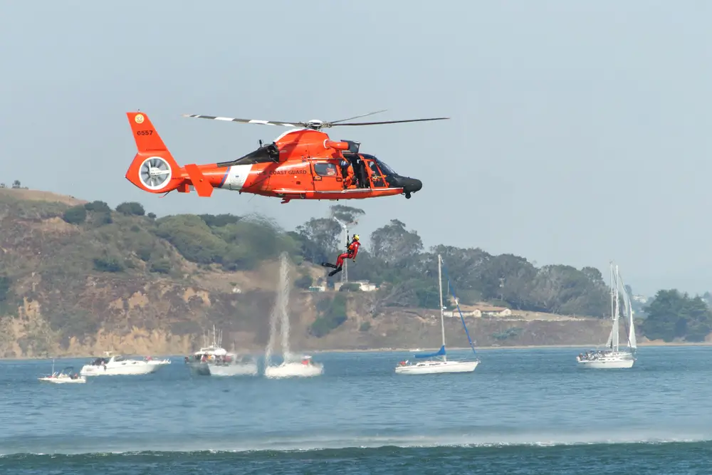 Coast Guard rescue swimmer in wetsuit being deployed from helicopter over ocean