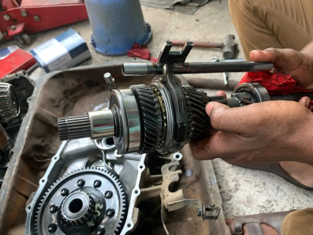 Mechanic trainee gear assembly being held, showing complex interlocking transmission gears in a vehicle workshop.