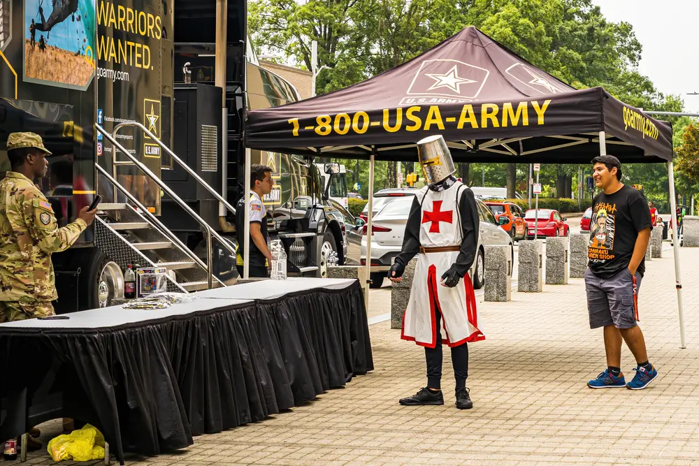 Military recruiter and civilian candidate at an outdoor Army enlistment event with a person in a medieval knight costume.