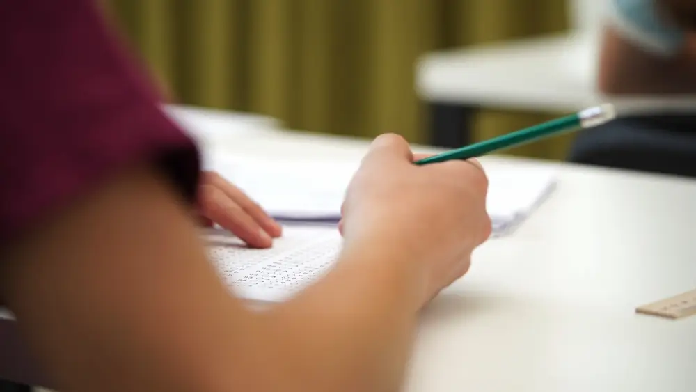 Students seated at desks taking a standardized pencil and paper exam in a testing room