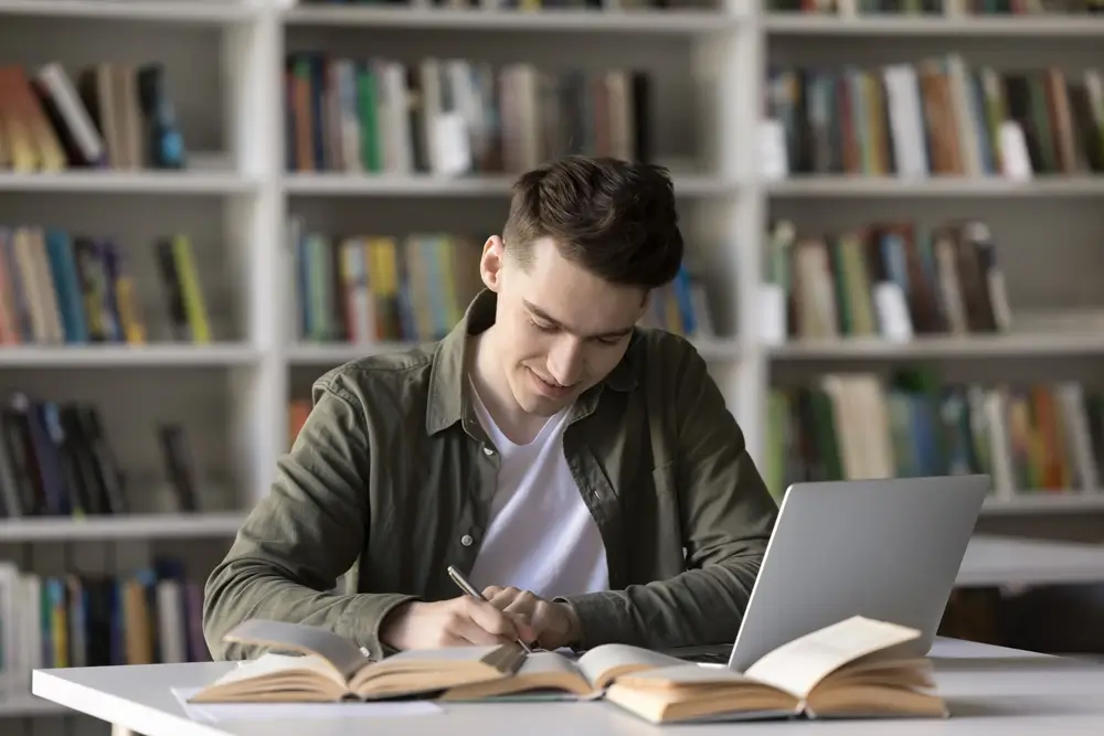 Student studying at a desk with open textbooks and notes preparing for a military exam