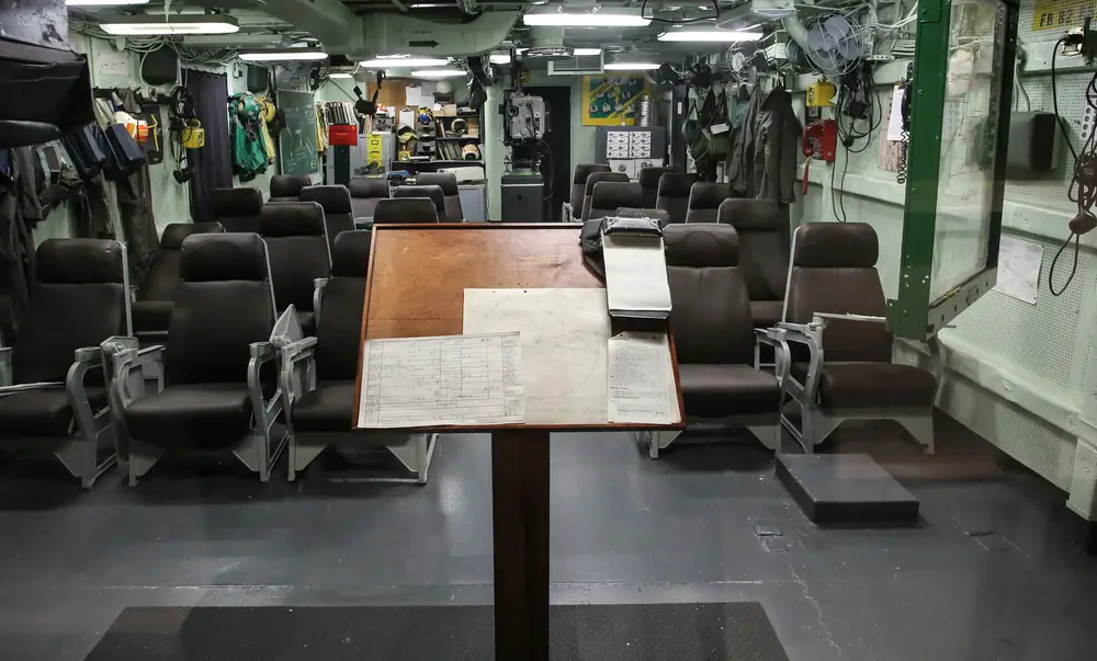 Technical charts on a podium in a submarine control room with seating and navy equipment for nuclear technicians.