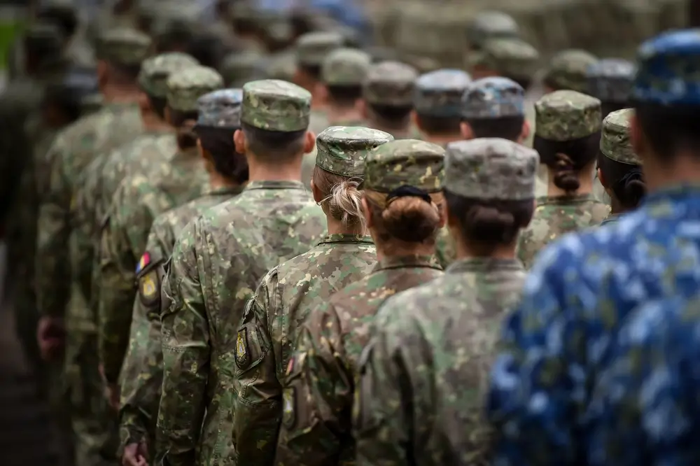 Military recruits in camouflage uniforms standing in formation outdoors.