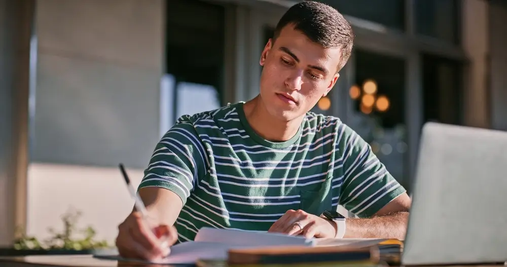 Student writing math formulas on scratch paper at desk preparing for a military enlistment exam