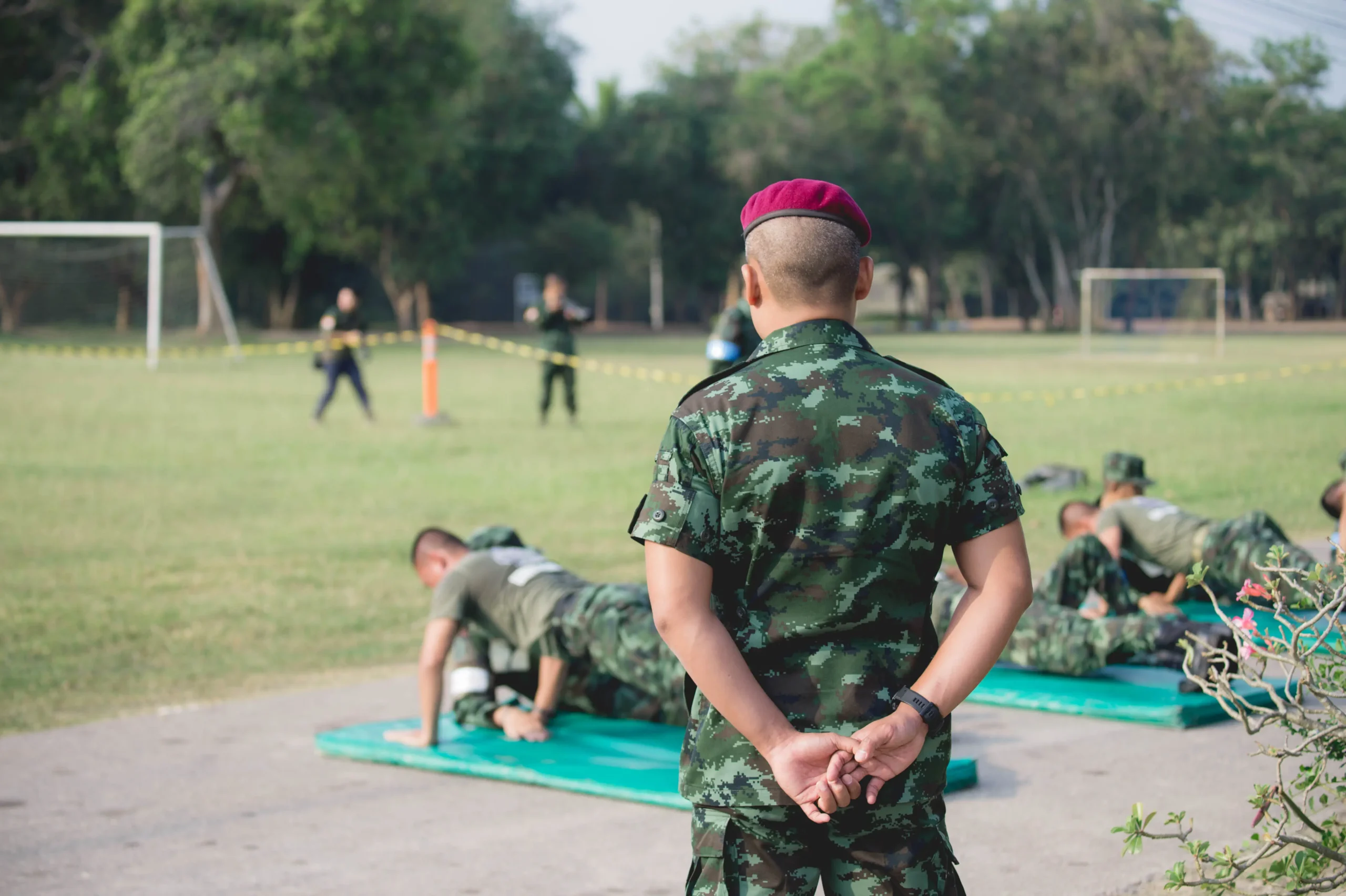 Military recruits performing fitness exercises on mats under supervision during outdoor training.
