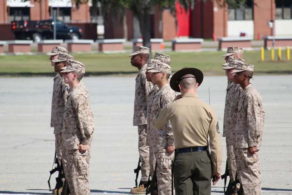Marine Corps recruits stand at attention in formation during military training with a drill instructor.