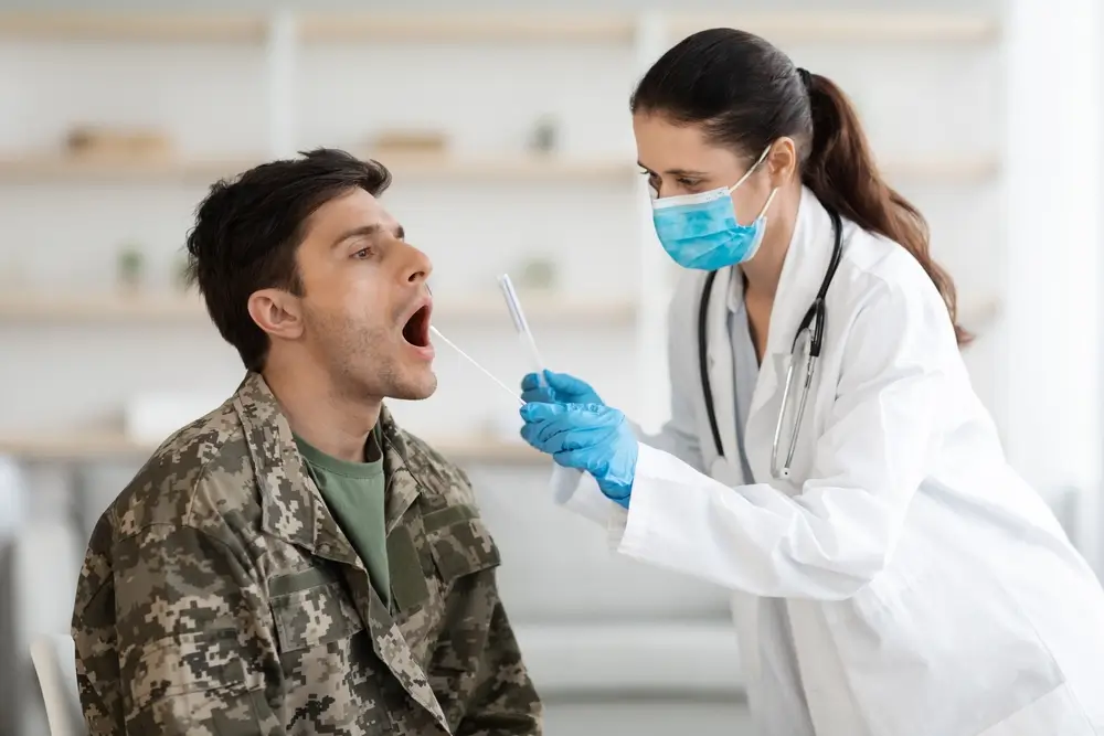 Military applicant in camouflage receiving a throat swab from a doctor during a MEPS medical exam.