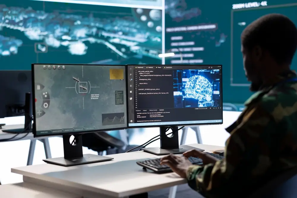 Military operator monitoring data and code on multiple screens in a satellite control room.