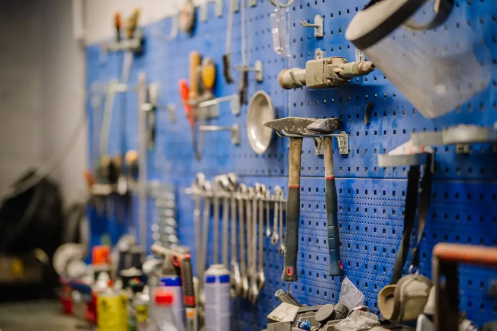 Assorted hand tools including wrenches and hammers hanging on a blue pegboard in a mechanical workshop.
