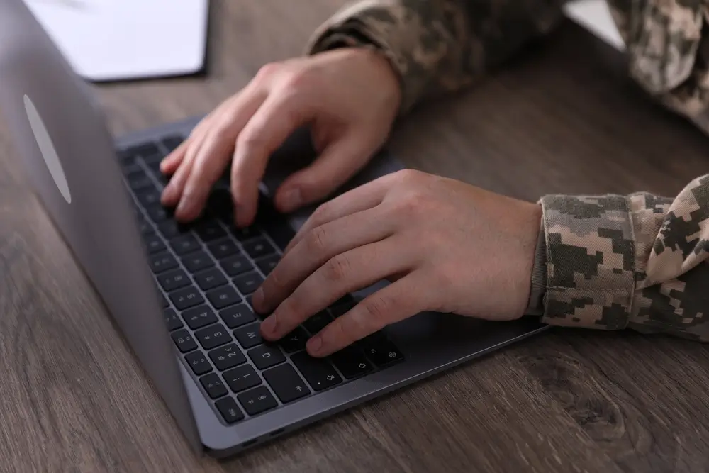Soldier in uniform studying on a military laptop, researching ASVAB scores and job qualifications.