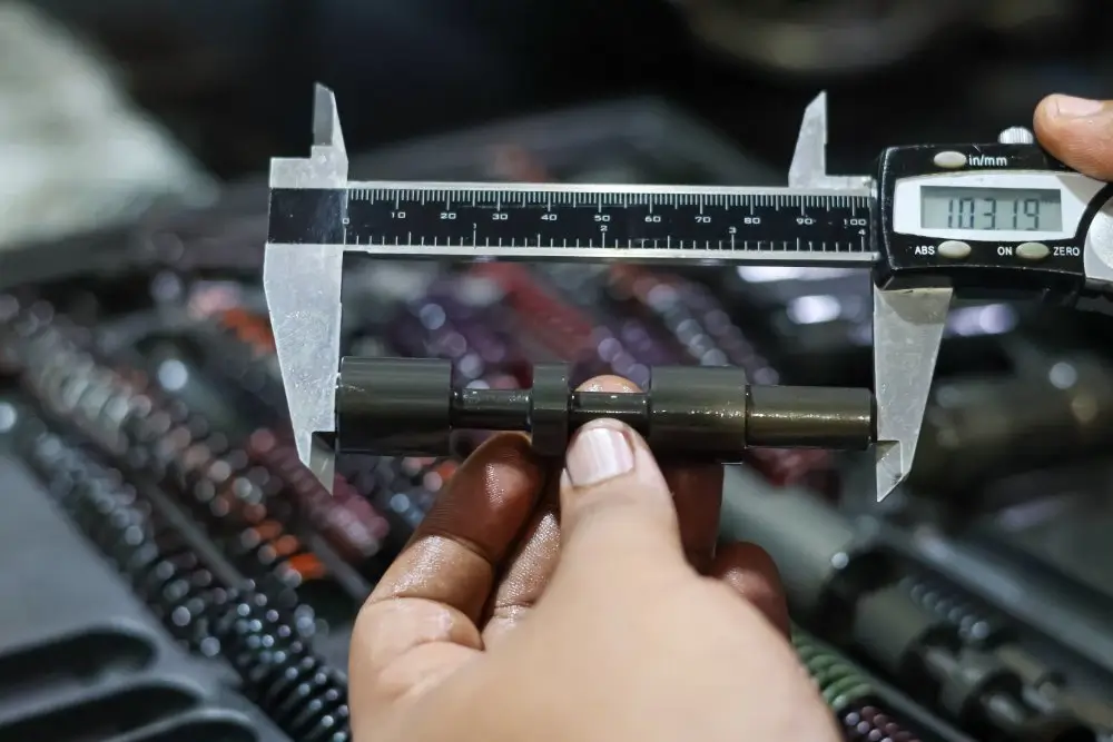Technician performing a micrometer precision measurement on a metal component using a digital caliper in a workshop.