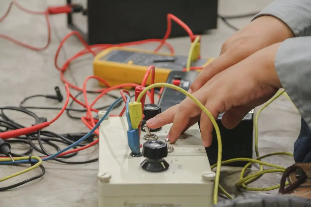 Military technician testing an electrical circuit with a multimeter and toggle switches on a workbench.